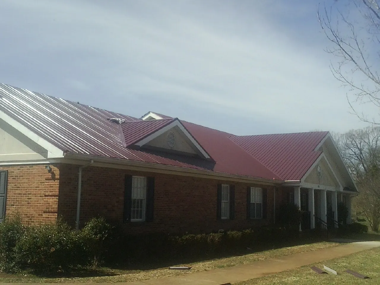 Red metal roof with gabled entries on a long brick building, from a Hail Damage Roof Repair job in Millerton