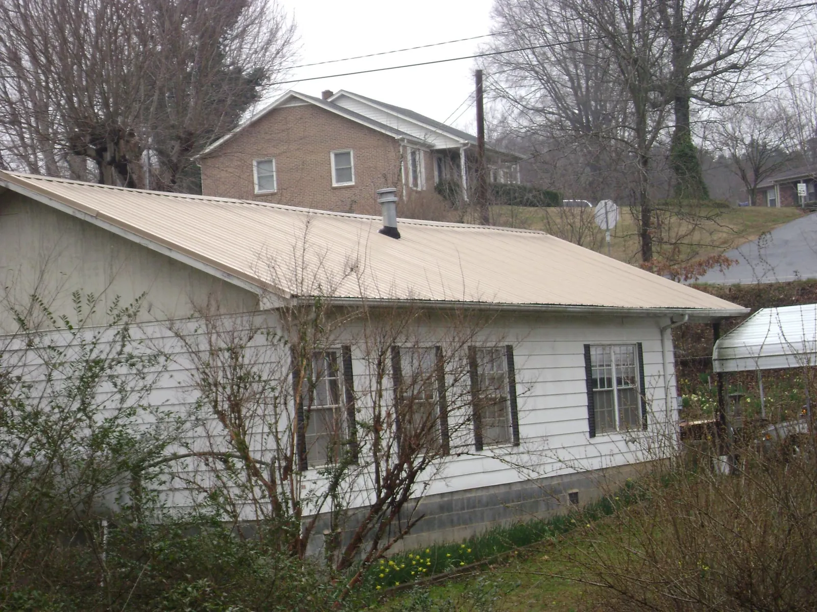 Tan metal roof on a white sided house set into a hillside — Commercial Roofing by Roofing Brothers in Millerton